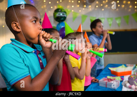 Children blowing party horns while standing by table during birthday party Stock Photo