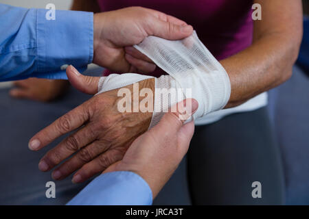 Physiotherapist putting bandage on injured hand of patient in clinic Stock Photo