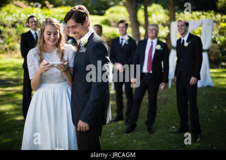 Bride and groom reviewing photographs on mobile phone during wedding Stock Photo