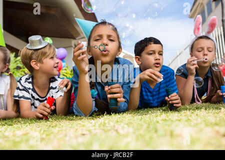 Children blowing bubbles while lying on field in yard Stock Photo