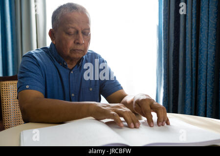 Senior man reading braille book at table in retirement home Stock Photo