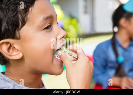 Close up of boy eating cake with friend in background during birthday party Stock Photo