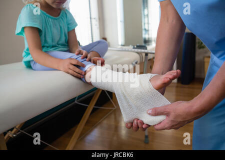 Physiotherapist putting bandage on injured feet of girl patient in clinic Stock Photo