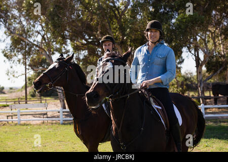 Two male friends riding horse in the ranch on a sunny day Stock Photo