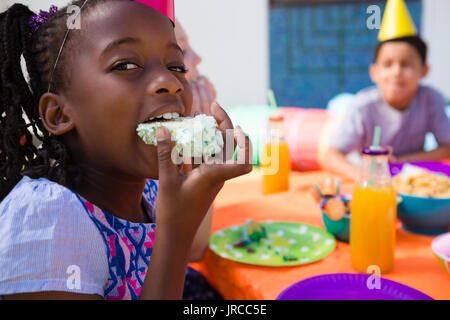 Portrait of girl eating cake with friends in background during birthday party Stock Photo