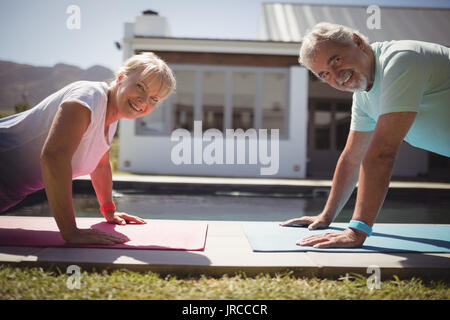 Portrait of smiling senior couple doing push-up near swimming pool on sunny day Stock Photo