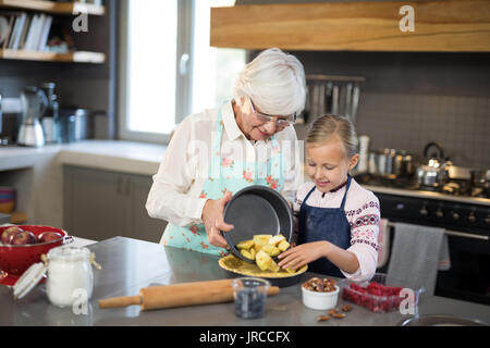 Grandmother and granddaughter adding fresh cut apples to the crust while making apple pie in the kitchen Stock Photo