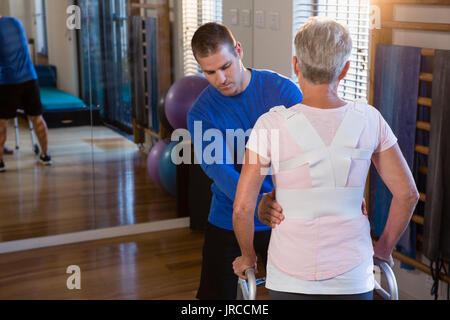 Physiotherapist assisting patient to walk with walking frame in clinic Stock Photo