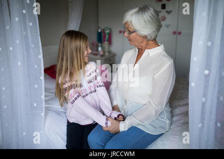 Smiling grandmother and granddaughter interacting with each other on bed in bedroom Stock Photo