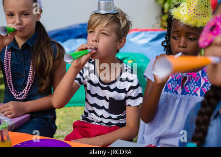 Children blowing part horns during birthday in yard Stock Photo