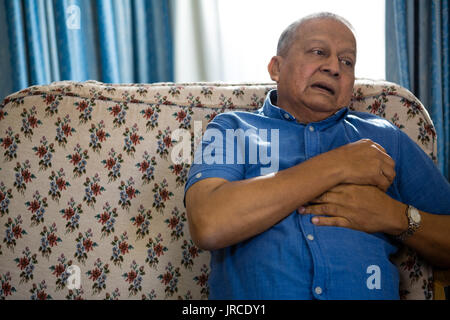 Sad thoughtful senior man looking away while sitting on sofa in nursing home Stock Photo