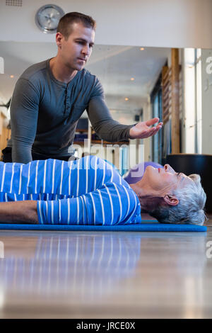 Physiotherapist assisting senior woman in performing exercise on mat at clinic Stock Photo