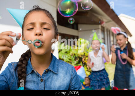 Girl blowing bubbles while standing in yard Stock Photo