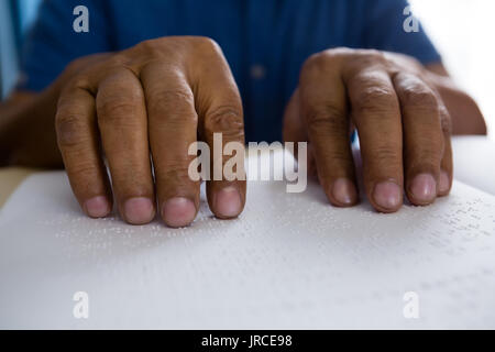 idsection of senior man reading braille book at table in nursing home Stock Photo