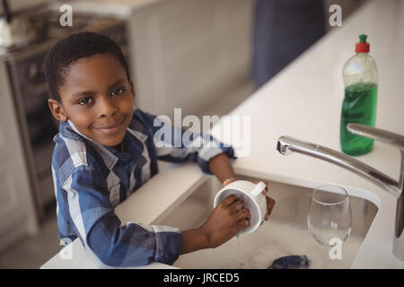 Portrait of smiling boy washing cup in kitchen sink at home Stock Photo