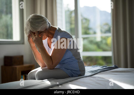 Tense senior woman sitting on bed in bedroom at home Stock Photo