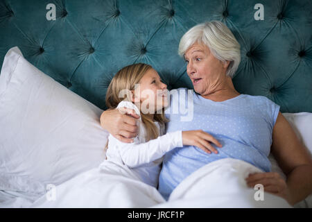 Smiling grandmother and granddaughter interacting with each other on bed Stock Photo