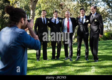 Photographer taking photo of groom and groomsmen at park Stock Photo