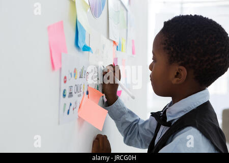 Side view of businessman writing on paper at whiteboard in creative office Stock Photo