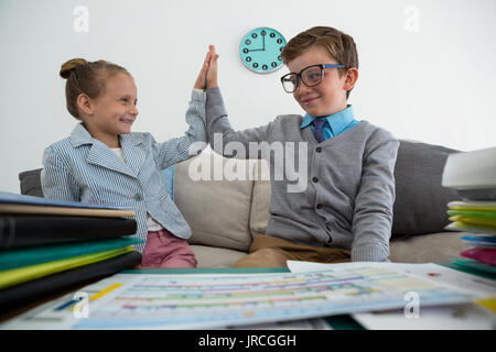 Smiling colleagues giving high five while sitting on sofa in office Stock Photo