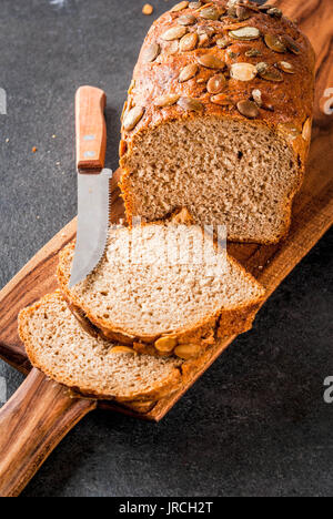 Freshly baked homemade organic multi-grain bread with pumpkin seeds on a cutting board on a black stone table. Copy space Stock Photo