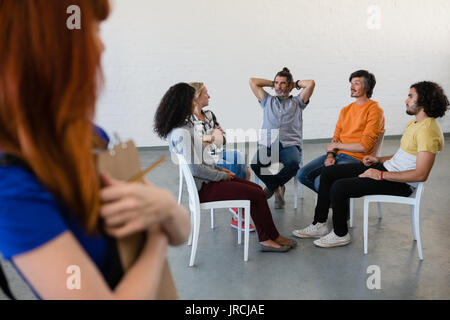 Side view of female teacher looking at students talking while sitting on chair in art class Stock Photo