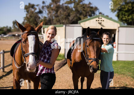 Portrait female friends with horses standing on field against barn Stock Photo