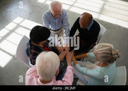 High angle view of senior friends stacking hands while sitting on chair in art class Stock Photo