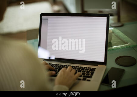 Cropped image of woman using laptop at table in kitchen Stock Photo