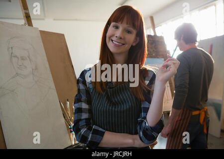 Portrait of woman holding paintbrush while standing by painting Stock Photo