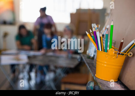 Close up of colored pencils in bucket on easel with students in background at art class Stock Photo