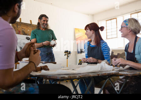 Smiling adult student looking at teacher explaining while standing in art class Stock Photo