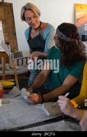Smiling teacher holding laptop while guiding student in art class Stock Photo