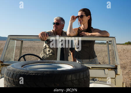 Couple looking away while standing in vehicle on landscape during sunny day Stock Photo