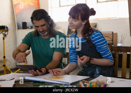 Teacher showing tablet computer to student at table in art class Stock Photo