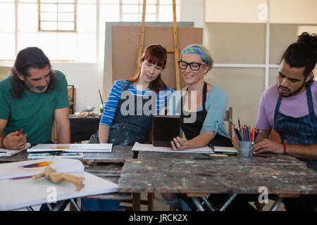 Smiling teacher showing tablet computer to adult students while practicing in art calss Stock Photo