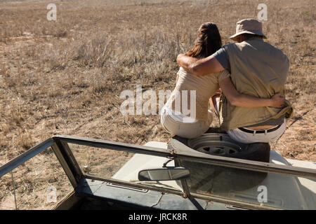 Rear view of couple sitting on spare tire over vehicle hood at landscape Stock Photo