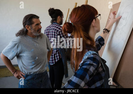 Man looking at female friend sketching on artists canvas in art class Stock Photo