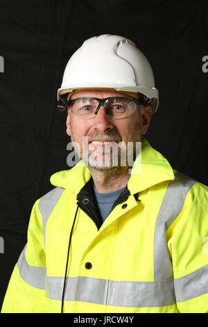 A construction worker in yellow high-viz jacket smiles at the camera. Plain dark background. Stock Photo