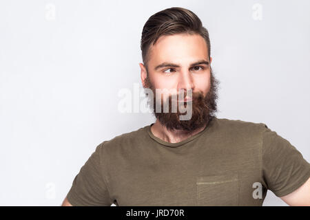 Portrait of crazy cross eyed bearded man with dark green t shirt against light gray background. studio shot. Stock Photo