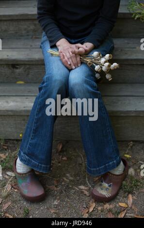 A person sitting on steps holding a bouquet of dried poppies. Stock Photo