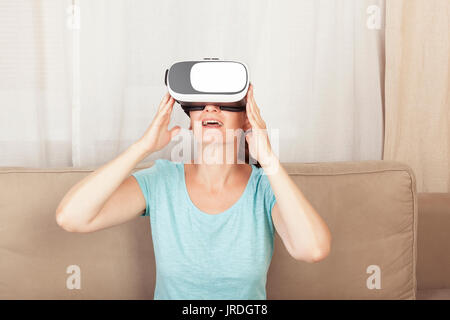 Beautiful women using virtual relaity glasses in living room at home. Future of entertainment. Virtual reality. Stock Photo