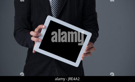 Businessman holding tablet in black suit on gray background Stock Photo