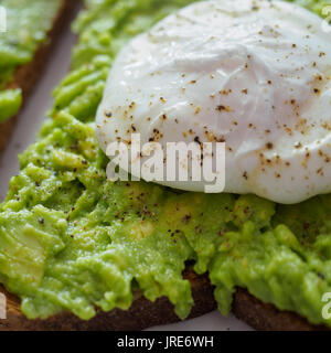 Close up of a poached egg on a smashed avocado toast with ground black pepper. Stock Photo