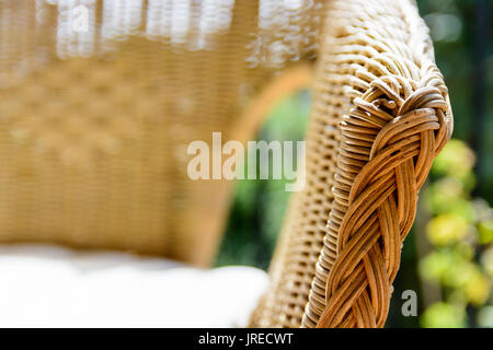 Close-up view on the armrest of a rattan armchair with a white cushion in the sunlight on a balcony with planter. Stock Photo