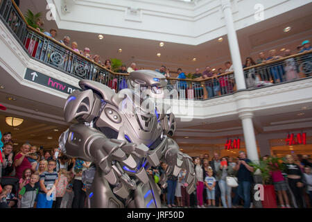 Preston, Lancashire, UK. Titan the robot, wearing an exoskeleton suit, wows the crowds at St George's Centre. Titan is the stage name of a partially-mechanised costume created by Cyberstein Robots Ltd. The robot costume is approximately 2.4 metres (7.9 ft) tall and 60 kg and increases to 350 kg including the cart it rides on and onboard equipment. The face resembles a skull, and some have even compared it to a Transformer. It was designed by Nik Fielding, who runs Cyberstein from Newquay, Cornwall, England. Stock Photo