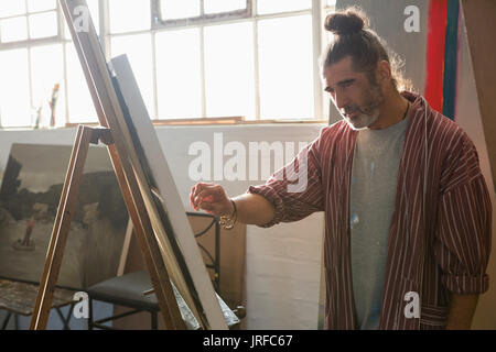 Mature man painting on easel by window in art class Stock Photo
