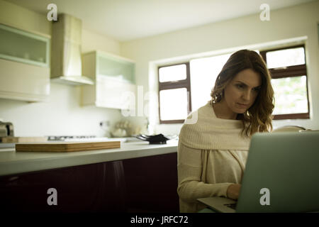 Woman using laptop in kitchen at home Stock Photo
