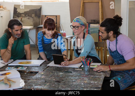 Woman showing tablet computer to adult students while practicing in art calss Stock Photo