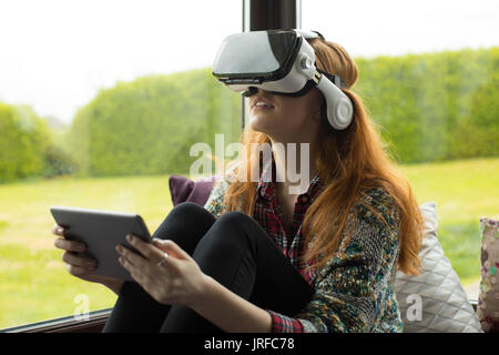 Young woman using vr glasses while sitting on alcove window seat at home Stock Photo